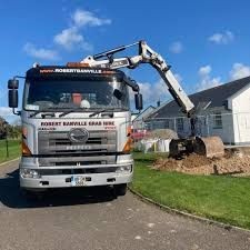 Construction truck with grab arm parked near a pile of dirt by a house on a sunny day.