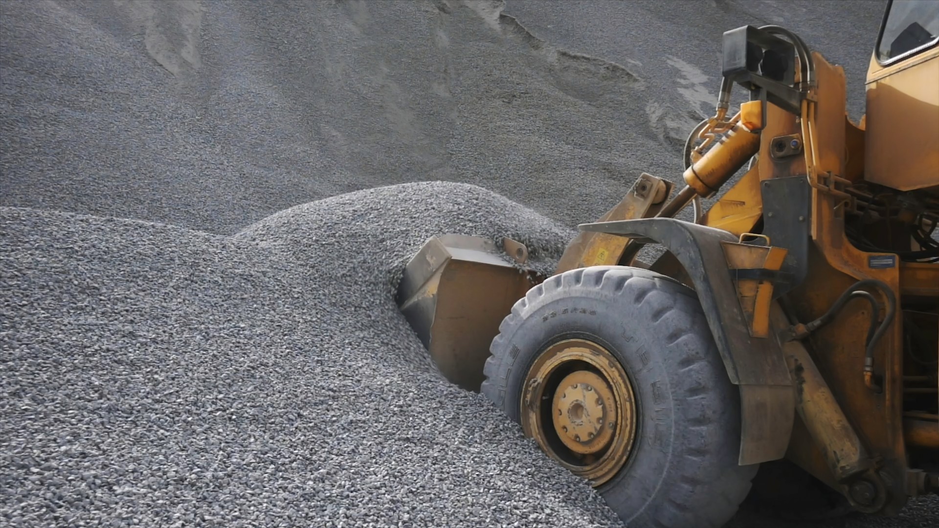 The tractor collects a scoop with gravel. Stock footage. Side view of an excavator loading its bucket with crushed stones or rubble at the construction site.